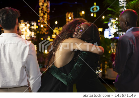 Close up of smiling women sharing affectionate hug during New Year Eve rooftop party at night. Jolly friends embracing each other during emotional festive midnight moment Close up of smiling women sharing affectionate hug during New Year Eve rooftop party at night. Jolly friends embracing each other during emotional festive midnight moment 143671149