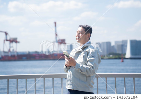 一名身穿工作服的男子手持智慧型手機 一名身穿工作服的男子手持智慧型手機 143672194