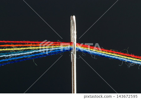 multi-colored threads for sewing in the form of a rainbow pass through an antique needle on a black background multi-colored threads for sewing in the form of a rainbow pass through an antique needle on a black background 143672595