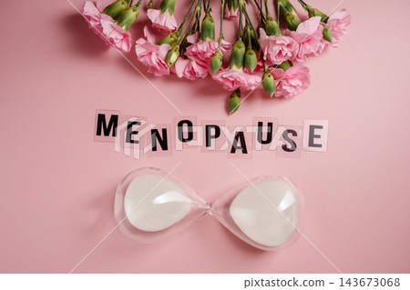 Menopause concept with hourglass and pink carnations on pastel background Menopause concept with hourglass and pink carnations on pastel background 143673068