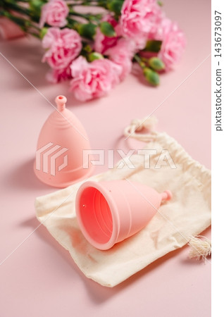 Reusable menstrual cups with cotton storage pouch and pink carnations on pink background Reusable menstrual cups with cotton storage pouch and pink carnations on pink background 143673097