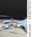 A scene of the airport apron illuminated by nighttime lights, with parked airplanes and service vehicles. 143673533