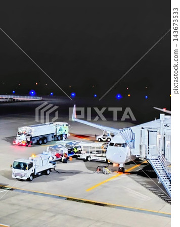A scene of the airport apron illuminated by nighttime lights, with parked airplanes and service vehicles. 143673533