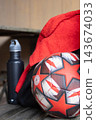 Soccer ball, water bottle and red towel resting on wooden bench, symbolizing preparation for sports training, fitness, and active lifestyle 143674033
