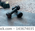 Home fitness equipment with dumbbells and ankle weights resting on a yoga mat, preparing for a workout session and promoting a healthy lifestyle and wellbeing 143674035