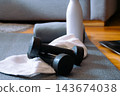 Dumbbells resting on a white towel on a yoga mat, with a white water bottle and an open laptop in the background, signifying modern home fitness, personal wellness, and digital workout routines. 143674038