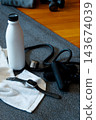 Fitness equipment arranged on a yoga mat, including a smartwatch, water bottle, and resistance band, promoting health, workout, and wellness at home 143674039