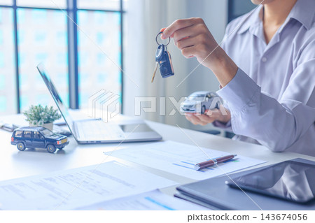 Car salesman handing over keys to client at dealership desk for new auto loan approval. Car salesman handing over keys to client at dealership desk for new auto loan approval. 143674056