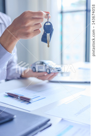 Car salesman handing over keys to client at dealership desk for new auto loan approval. Car salesman handing over keys to client at dealership desk for new auto loan approval. 143674058