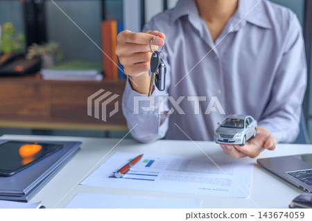 Car salesman handing over keys to client at dealership desk for new auto loan approval. Car salesman handing over keys to client at dealership desk for new auto loan approval. 143674059