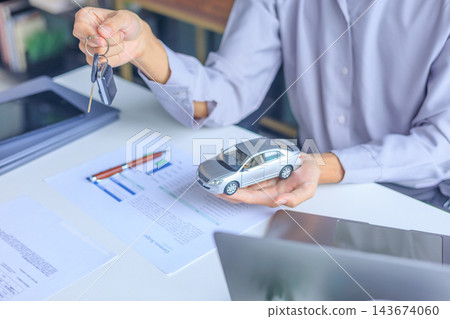 Car salesman handing over keys to client at dealership desk for new auto loan approval. Car salesman handing over keys to client at dealership desk for new auto loan approval. 143674060