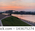 A view of the riverbank and bridge at dusk. 143675274