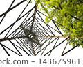 A low-angle view looking up at a lattice steel tower with green leaves . 143675961