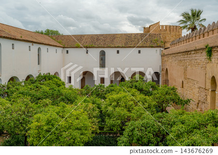 Whitewashed arcaded courtyard with orange trees and crenellated fortress wall at the Alcazar of Cordoba Whitewashed arcaded courtyard with orange trees and crenellated fortress wall at the Alcazar of Cordoba 143676269