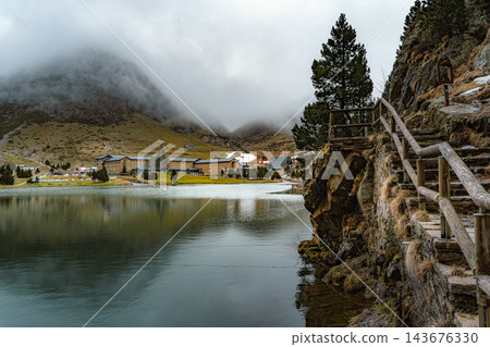 Wooden stairs with handrail beside a rock face on a mountain lake with sanctuary in the mist in Vall de Nuria Wooden stairs with handrail beside a rock face on a mountain lake with sanctuary in the mist in Vall de Nuria 143676330