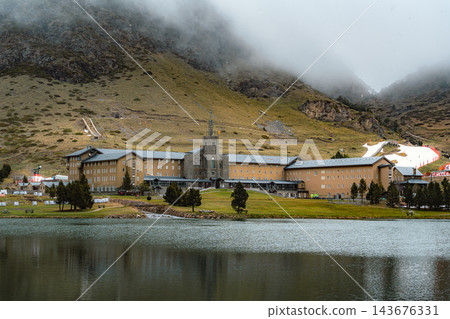 Large mountain sanctuary mirrored in a calm lake under fog covered mountain in Vall de Nuria Large mountain sanctuary mirrored in a calm lake under fog covered mountain in Vall de Nuria 143676331
