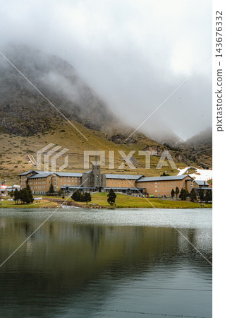Large mountain sanctuary mirrored in a calm lake under fog covered mountain in Vall de Nuria 143676332