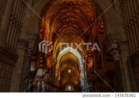 Gothic ribbed vault ceiling above red and white striped arches in a warmly lit aisle of the Mezquita of Cordoba Gothic ribbed vault ceiling above red and white striped arches in a warmly lit aisle of the Mezquita of Cordoba 143676362