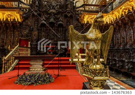 Golden eagle lectern in front of ornate carved choir stalls and red carpeted steps in the Mezquita of Cordoba 143676363