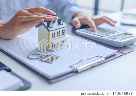 Businessman using calculator and touching miniature house with contract document on the table. Concept for real estate investment, loan, rent, mortgage, insurance Businessman using calculator and touching miniature house with contract document on the table. Concept for real estate investment, loan, rent, mortgage, insurance 143676988