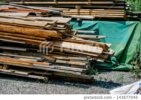Weathered wooden boards and lumber are stacked beside a protective tarp outdoors. Concept of construction, material reuse, storage and recycling. Weathered wooden boards and lumber are stacked beside a protective tarp outdoors. Concept of construction, material reuse, storage and recycling. 143677048