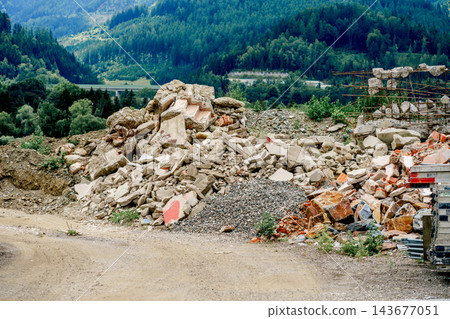 Broken concrete and bricks lie at a demolition site below forested mountains. Concept of construction, renovation, waste management and clearance. 143677051