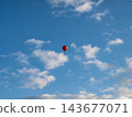 Bright Red Hot Air Balloon with Passengers Flying in Clear Blue Sky 143677071