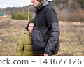 A smiling preteen boy hugs his father, feeling safe and protected during an autumn walk outdoors. 143677126