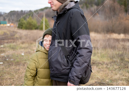 A smiling preteen boy hugs his father, feeling safe and protected during an autumn walk outdoors. 143677126