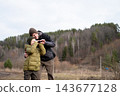 Father helping his preteen son looking through binoculars at forest scenery during autumn travel 143677128