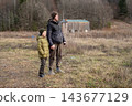 Father and preteen son holding hands and standing together in autumn field near old wooden barn 143677129