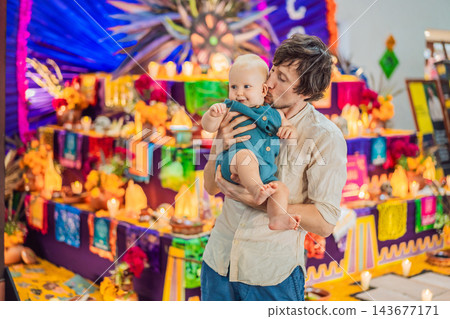 Father giving his baby a kiss beside a festive remembrance altar. 143677171