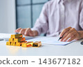 Selective focus on gold bars with background of hands using calculator for gold trading analysis. Concept for wealth management, asset protection, and financial planning. 143677182