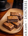 Stacked Homemade Chocolate Brownies on a Plate with Coffee Cup Close-Up in Cozy Cafe Setting 143678381