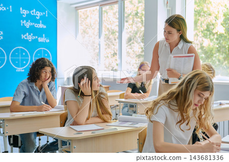 Math teacher helping teenage students at desk in classroom Math teacher helping teenage students at desk in classroom 143681336