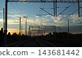 Electrified railway tracks with overhead lines and gantries at sunset, wind turbines in distance, sky copy space. Concept of rail transport, infrastructure, green transport, logistics, journey 143681442