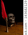 Human skull for Halloween, an image of a human skull in a macabre setting with an antique fountain pen featuring a red feather, selective focus. 143682129