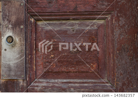 Old Brown Wooden Door with Metal Keyhole. Vintage wooden door with metal keyhole, scratched aged texture, worn paint, visible wood grain. Weathered wooden door background, rustic architectural detail 143682357