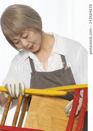 A senior woman remakes a doll chair in her living room as a DIY hobby. A senior woman remakes a doll chair in her living room as a DIY hobby. 143684876