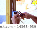 Hands use pliers to connect wires in an electrical box on wooden frame during repair. 143684939