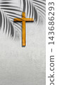A wooden Christian cross hangs on a textured grey wall with the shadow of palm leaves cast across it. Concept of Christian 143686293