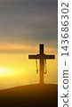 A silhouette of a Christian cross with a rosary draped over it stands on a hill against a vibrant sunrise or sunset sky, conveying spiritual devotion, faith, and hope. Concept of Christian 143686302