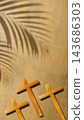 Three wooden crosses resting on sand with a palm frond shadow cast above, symbolizing the crucifixion and resurrection of Jesus Christ. Concept of Christian 143686303