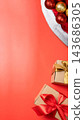 Christmas background on coral orange surface with Santa hat, gold and red ornaments, and wrapped gift boxes with ribbons. Top view with copy space. Concept of Merry Christmas 143686305