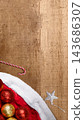 Christmas background with Santa's hat, shiny red and gold baubles, a candy cane, and a silver star on a rustic wooden texture. Concept of Merry Christmas 143686307