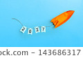 An orange origami rocket launches upward, towing a string of flags spelling the year 2027 against a vibrant blue background, symbolizing future growth, goals, and ambition. Concept of Happy New Year 143686317