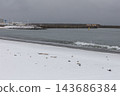 Winter waves crashing against the snow-covered sandy beach and the breakwater. 143686384