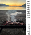 Close up of chef hands sprinkling sea salt on pork steaks grilling on a barbecue with flames below 143686628