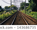 A rural railway line surrounded by greenery, with a station visible in the distance, and straight rails. 143686735