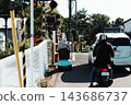The backs of cars, mopeds, and electric carts waiting at a closed railroad crossing. 143686737